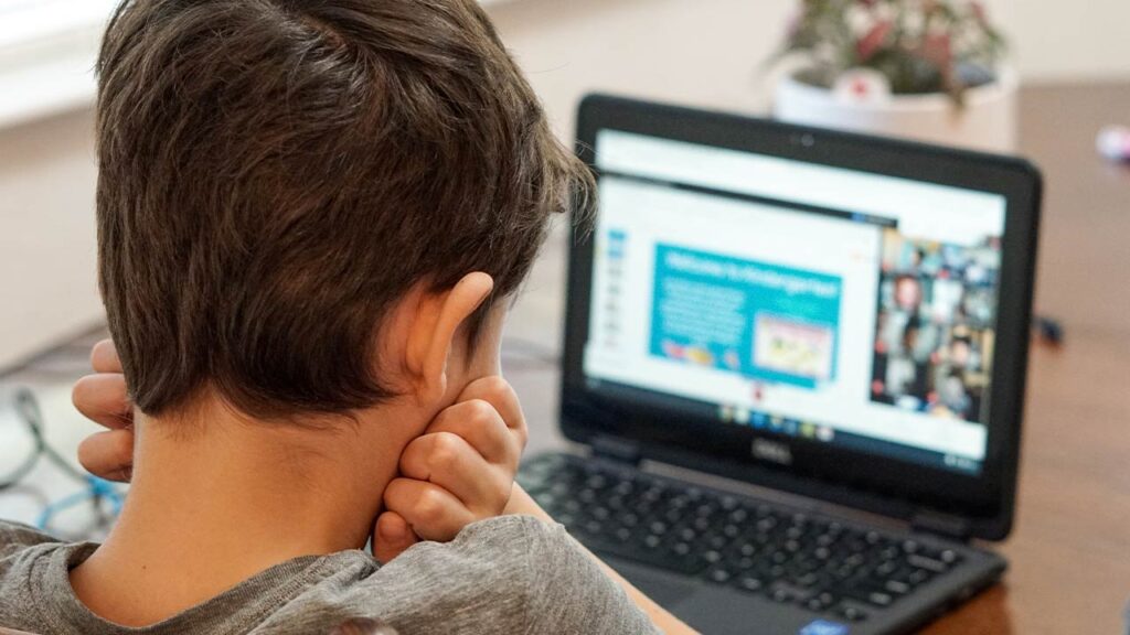 Dziecko siedziące tyłem przed ekranem laptopa, rękę trzyma przy policzku